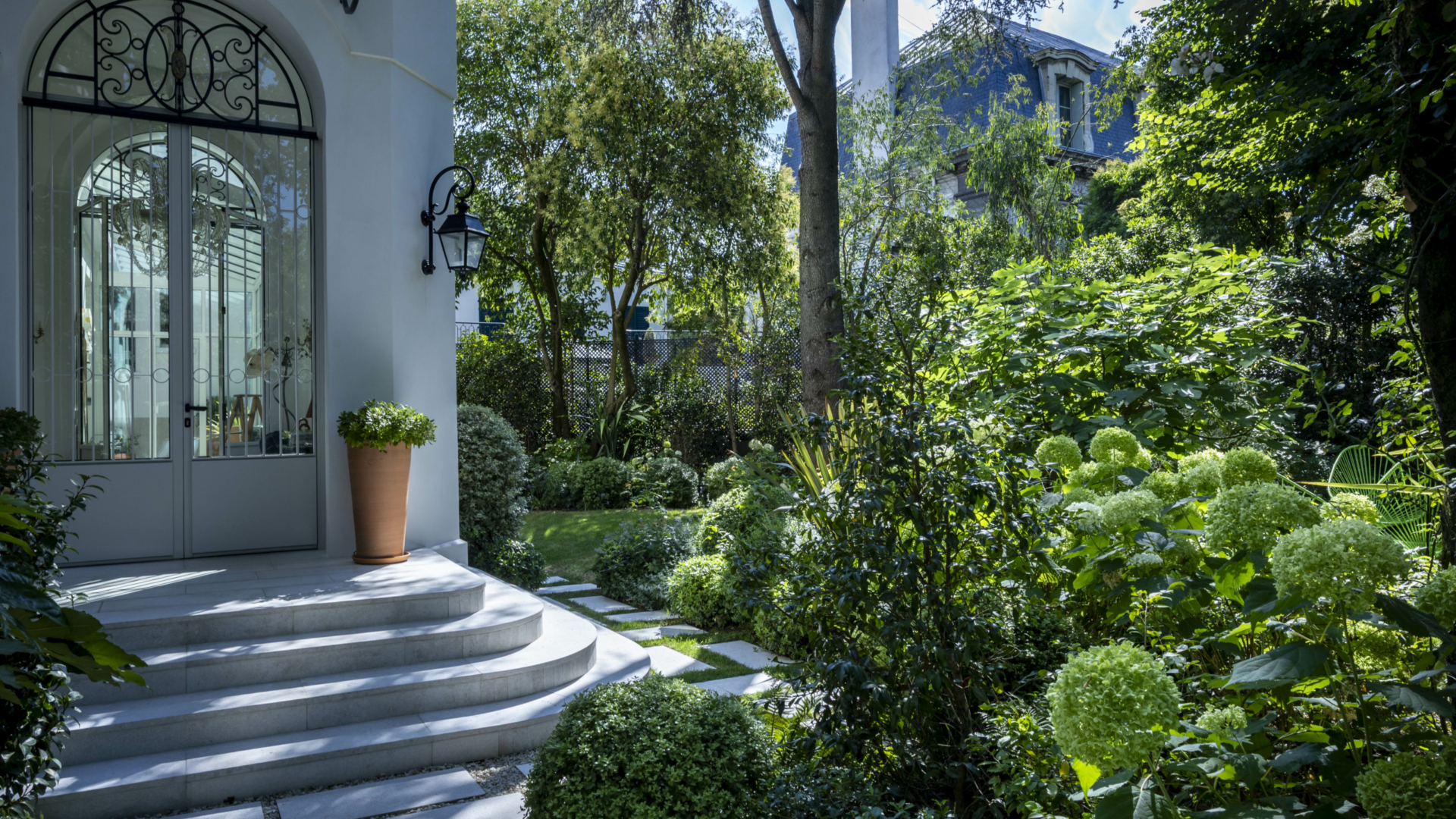 Aménagement d'un jardin à Paris réalisé en 2026 par notre bureau d'études paysager, avec allées en pas japonais, massifs fleuris, arbres d'ornement et végétation luxuriante autour d'une demeure de caractère.