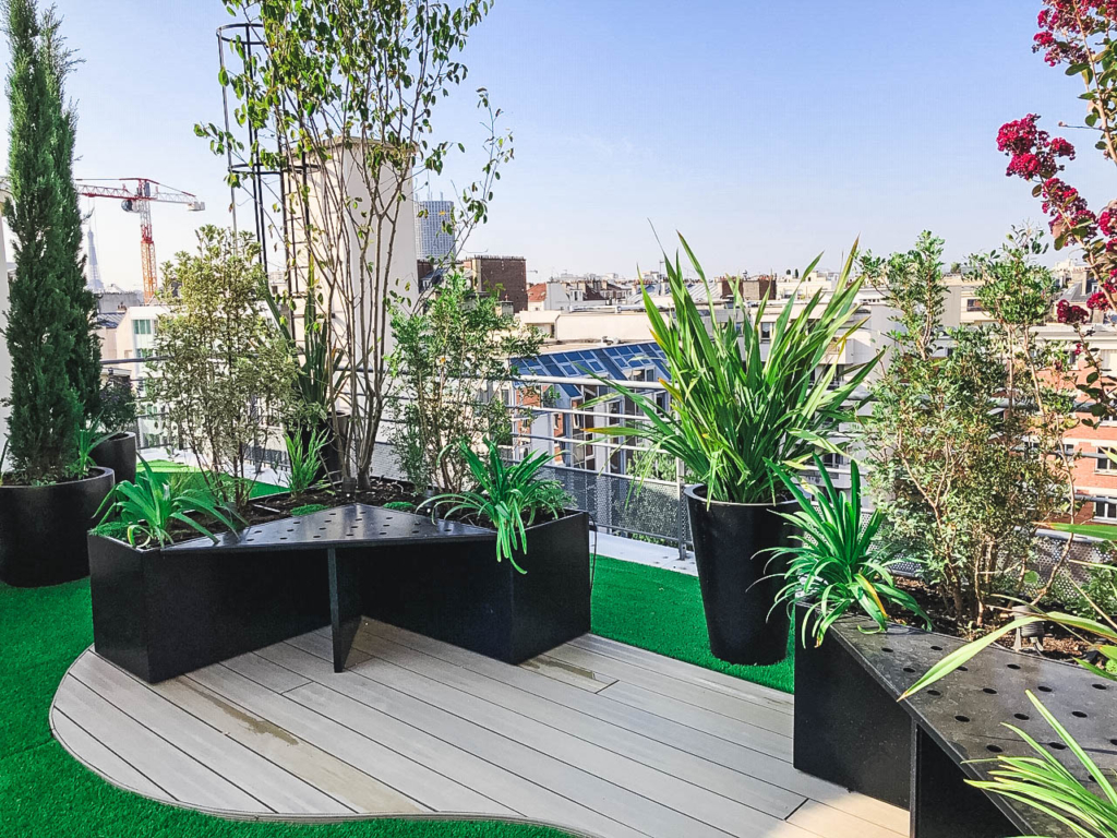 lmdj-amenagement-toit-terrasse-paris-3 Aménagement végétalisé d’un toit-terrasse parisien avec jardinières noires, banquettes intégrées et vue sur les toits de la ville.