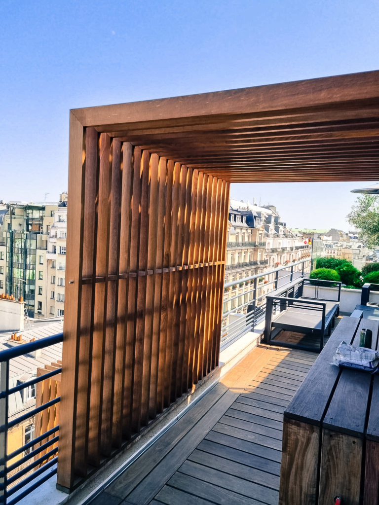 lmdj-amenagement-toit-terrasse-paris-7 Toit-terrasse à Paris avec claustra en bois vertical et mobilier extérieur assorti offrant une vue panoramique sur les toits.