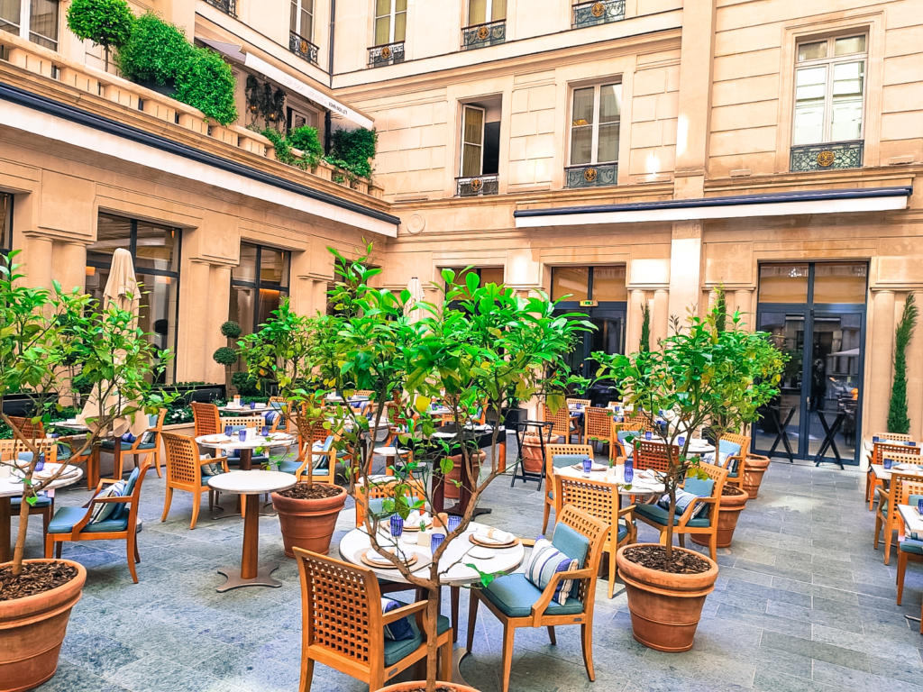 Patio parisien végétalisé avec tables de restaurant et orangers en pot dans un immeuble haussmannien.