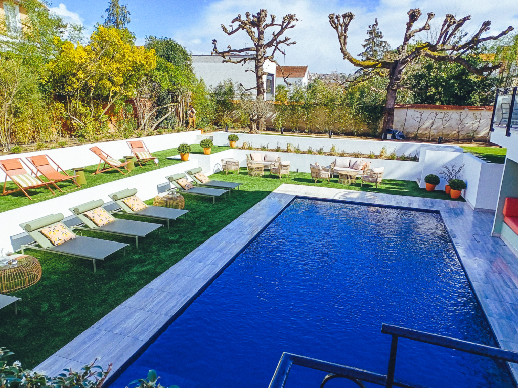 Piscine design entourée de transats et d’espaces lounge dans un jardin moderne.