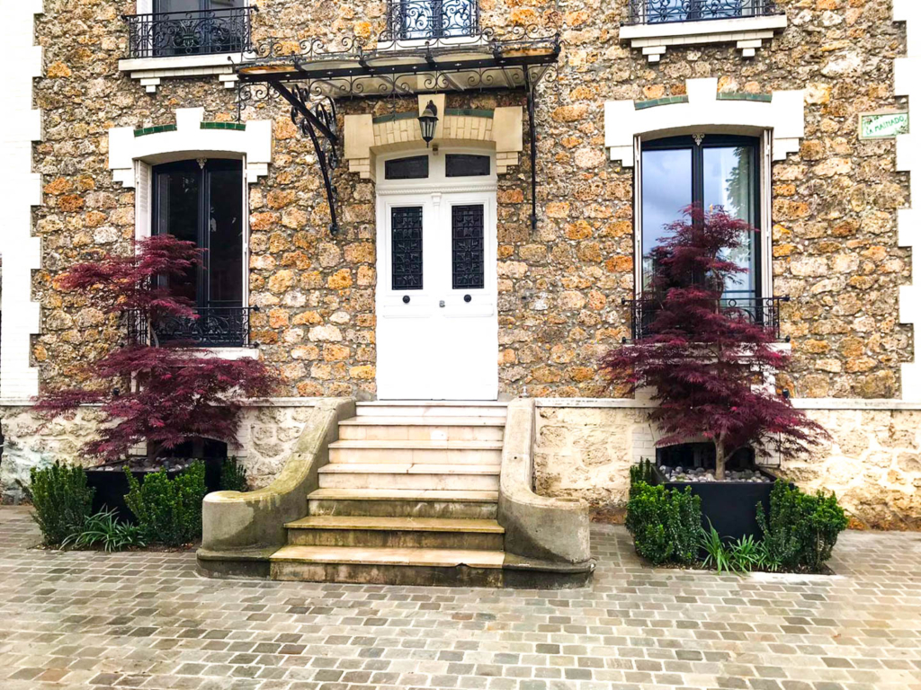 Entrée de maison en pierre avec escalier central, érables japonais et pavés.