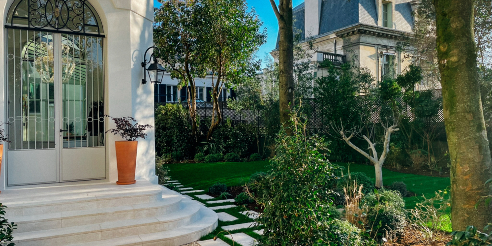 Aménagement paysager haut de gamme avec dalles en pierre, végétation maîtrisée et entrée de maison rénovée par un paysagiste-maçon.