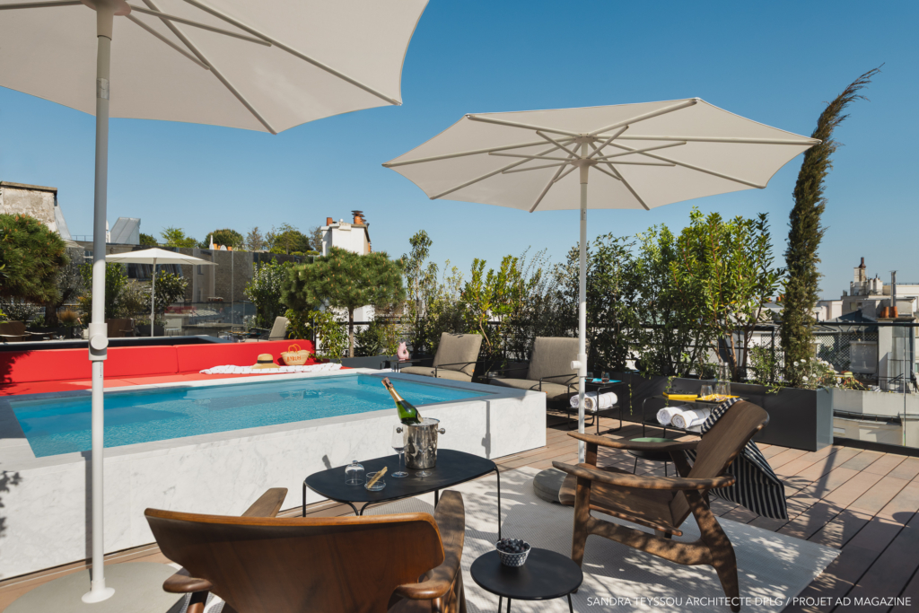 Piscine moderne sur rooftop avec banquette rouge, parasols et vue sur les toits de Paris.