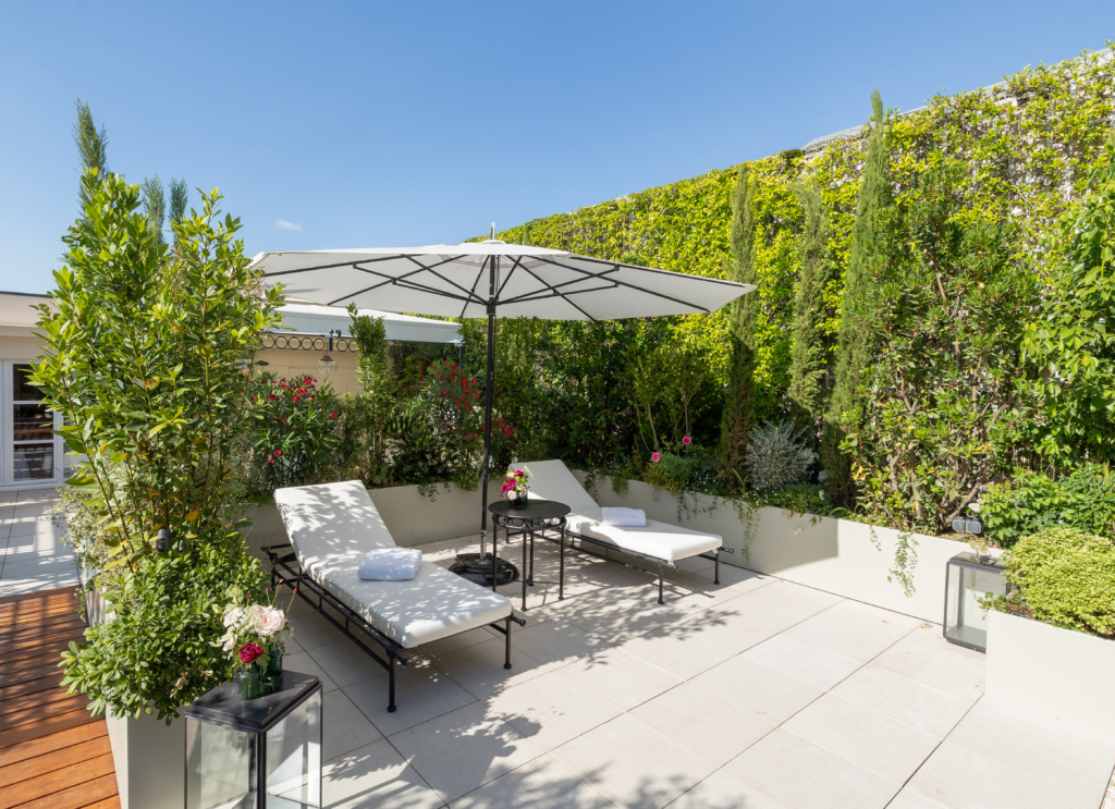 Terrasse en pierre naturelle avec transats, parasol et végétation luxuriante.