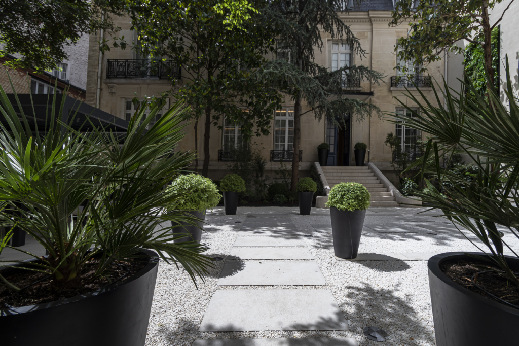 Cour élégante avec allée en pas japonais, pots décoratifs et façade classique en arrière-plan.