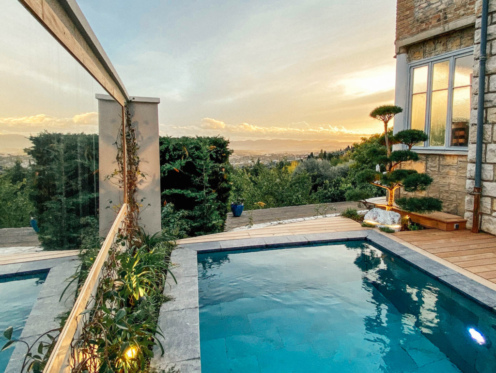 Piscine design avec terrasse en bois et vue panoramique sur le paysage au coucher du soleil.