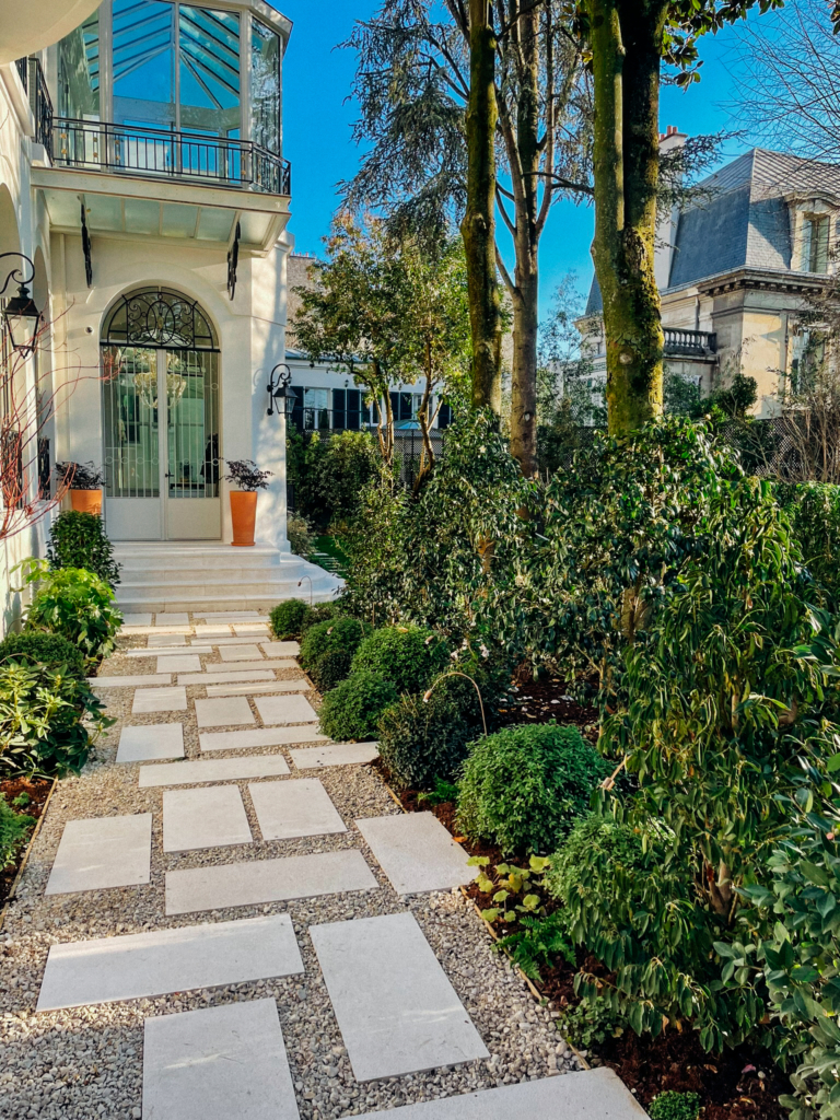 Allée paysagère réalisée par un paysagiste de demeure de prestige, avec pas japonais en pierre, massifs végétalisés et entrée élégante de propriété.