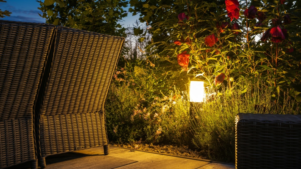Éclairage paysager nocturne mettant en valeur la végétation, le mobilier extérieur et l’atmosphère d’un jardin hôtelier.