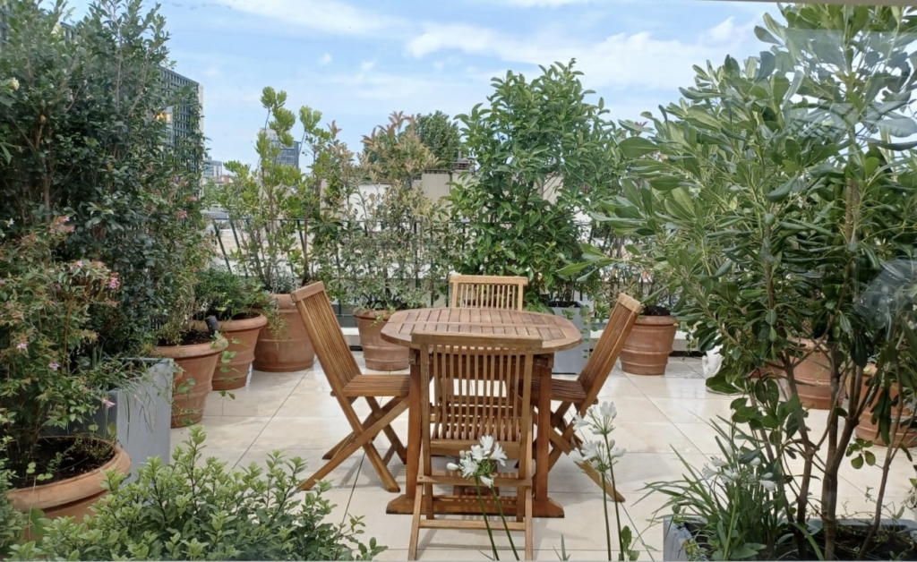 Terrasse urbaine avec table en bois et grandes plantes en pots créant un coin repas végétalisé