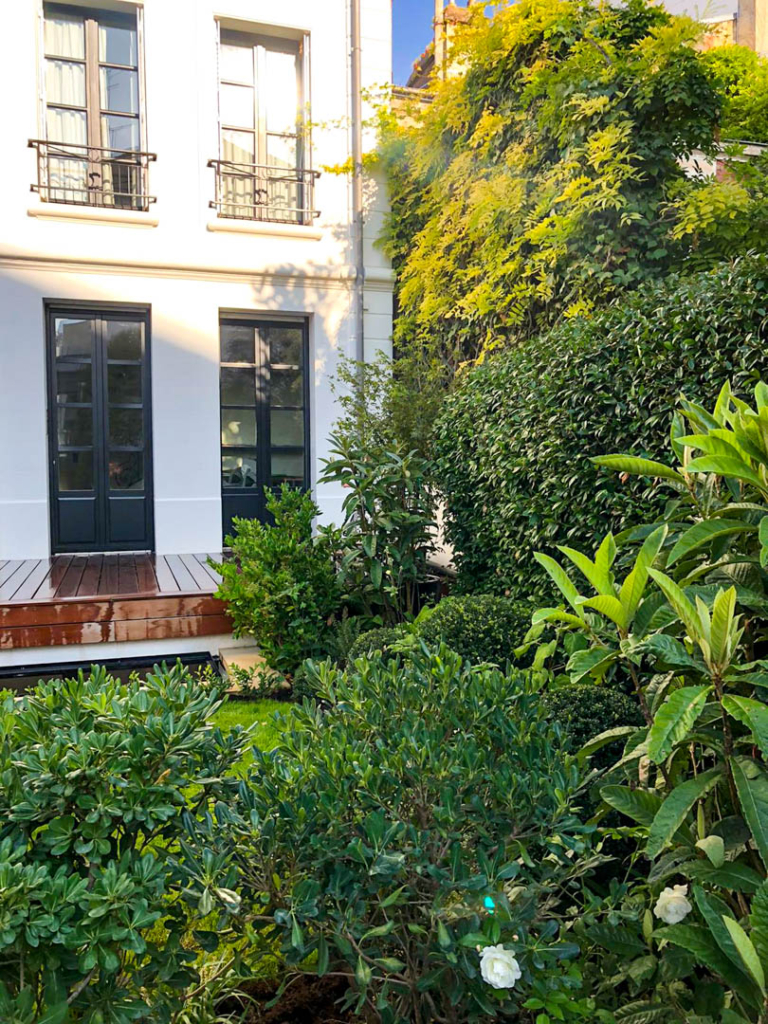 Jardin contemporain dans un lieu parisien avec terrasse en bois et végétation dense paysagée
