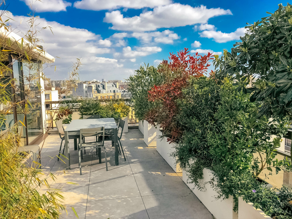Toit-terrasse végétalisé avec coin repas extérieur et jardinières luxuriantes en milieu urbain