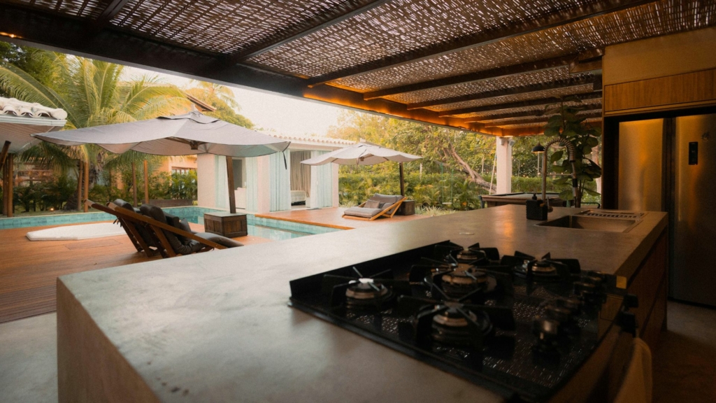 Espaces de vie Espaces de vie extérieurs avec cuisine d’été sous pergola, terrasse en bois, piscine, transats et aménagement paysager tropical haut de gamme.