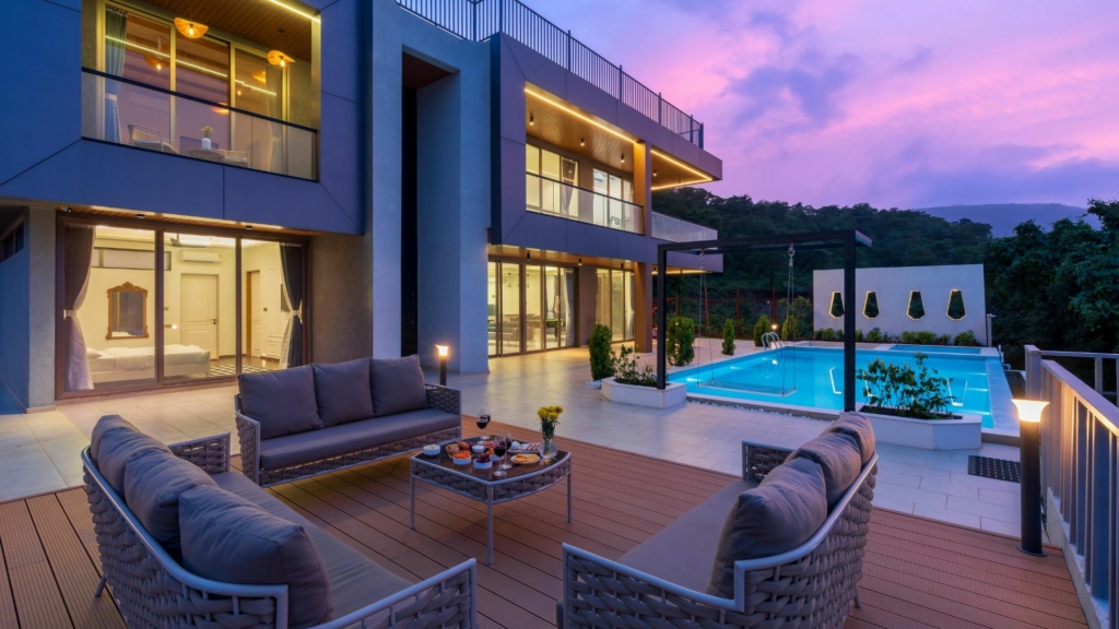 Terrasse contemporaine avec salon extérieur, piscine éclairée et aménagement paysager autour d’une villa moderne avec éclairage architectural.