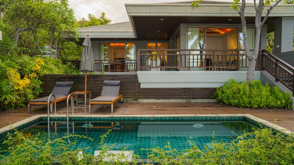 Aménagement d’un petit jardin avec piscine, terrasse en bois, transats et végétation dense autour d’une maison contemporaine.