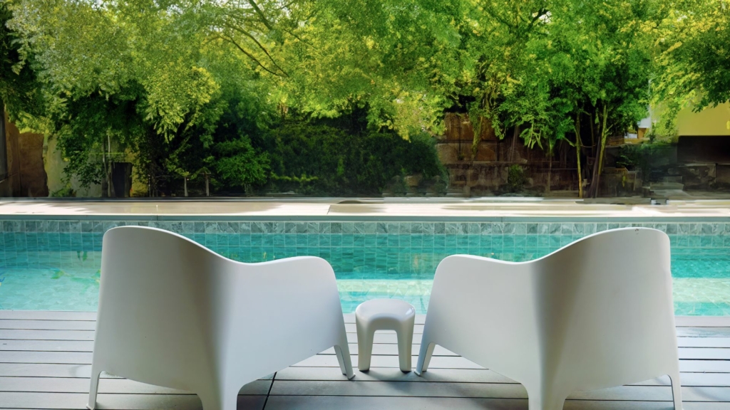 Terrasse avec fauteuils design face à une piscine, jardin arboré en arrière-plan et aménagement extérieur contemporain propice à la détente.