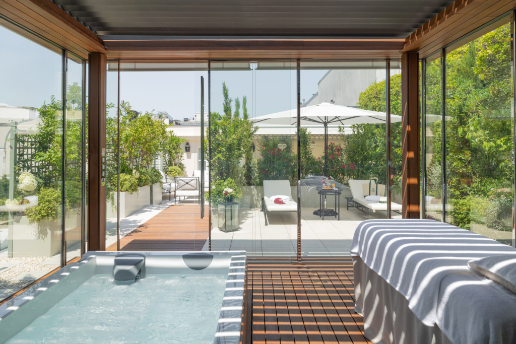 Suite Eden - terrasse ©Franck Bohbot _hUcYa (2) Pavillon spa vitré de la Suite Eden au Bristol Paris, avec un bain à remous et une table de massage, ouvert sur une terrasse plantée d'arbustes, de lauriers-roses et de jardinières