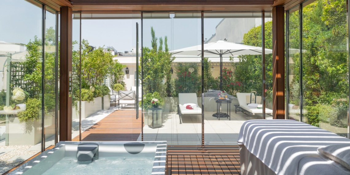Pavillon spa vitré de la Suite Eden au Bristol Paris, avec un bain à remous et une table de massage, ouvert sur une terrasse plantée d'arbustes, de lauriers-roses et de jardinières